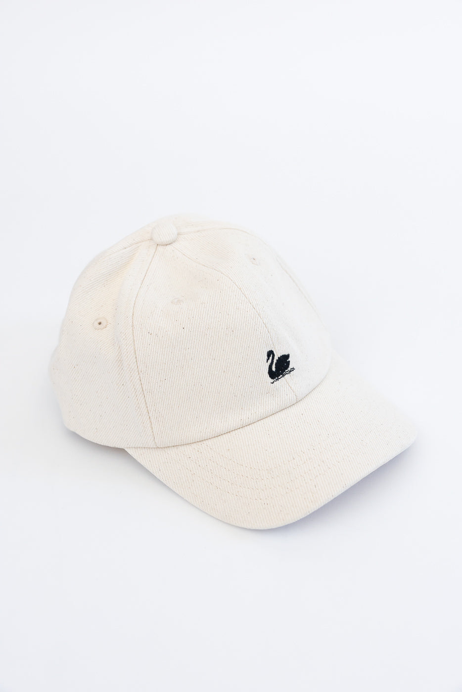 Close-up of front and top of natural cotton twill cap with black swan logo embroidery.