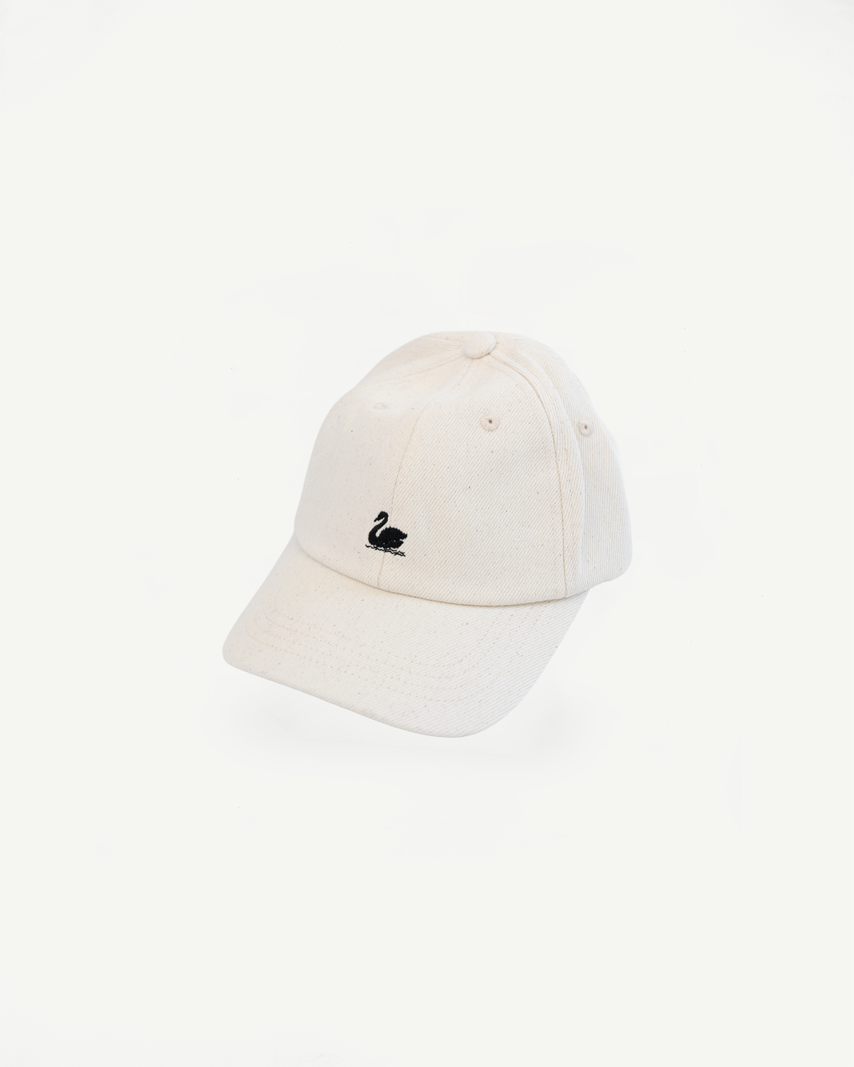 Front angled flat lay of natural cotton twill cap with black swan logo embroidery.