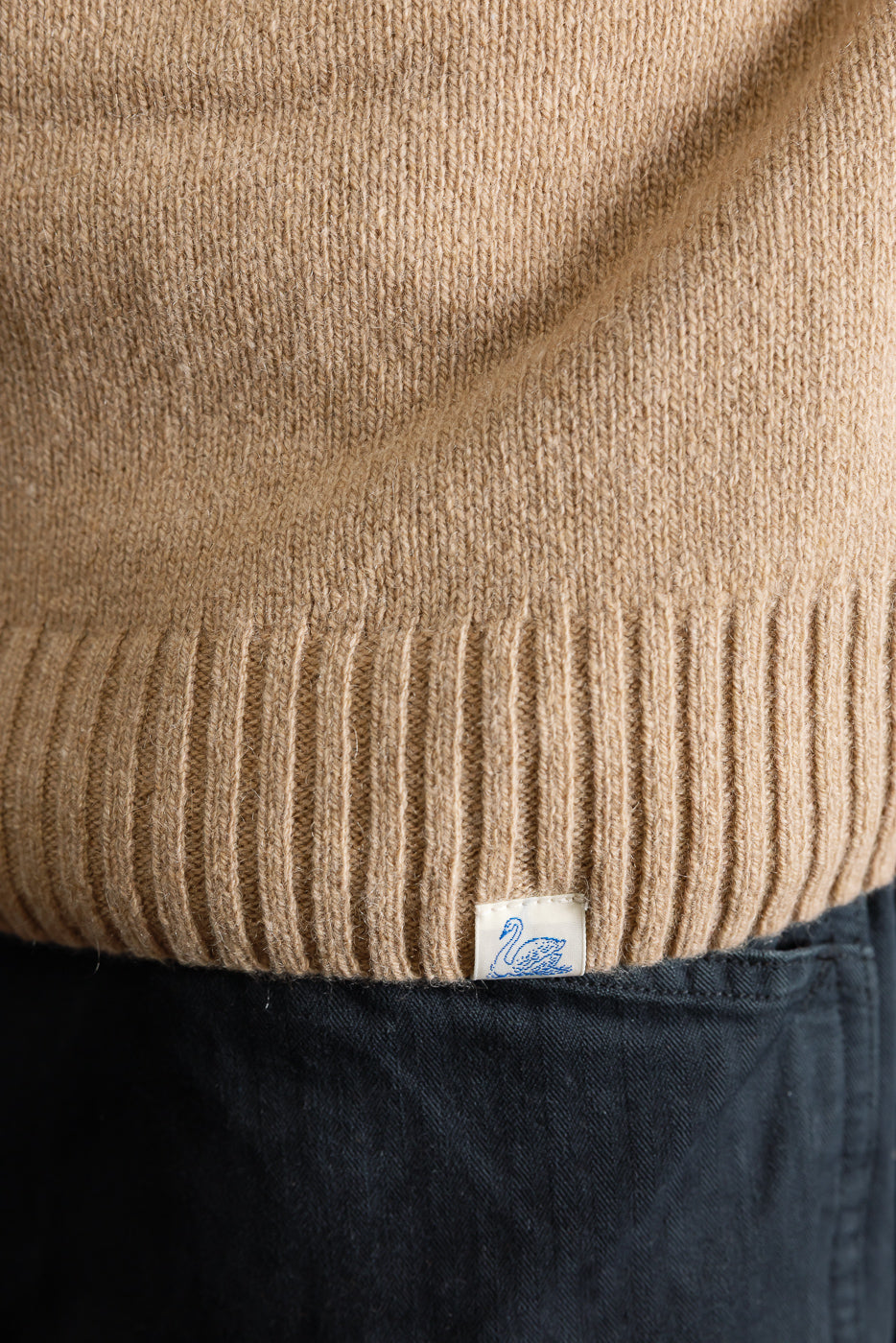 Close-up of male model wearing recycled cashmere sweater in toffee, front hem and ribbed texture with visible tag, 5'9