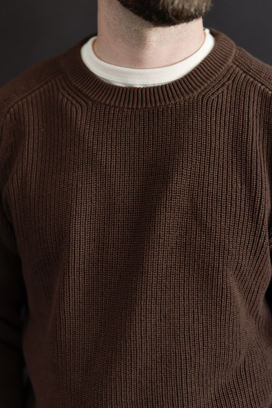 Close-up front view of a brown ribbed knit sweater collar and fabric texture on a male model.