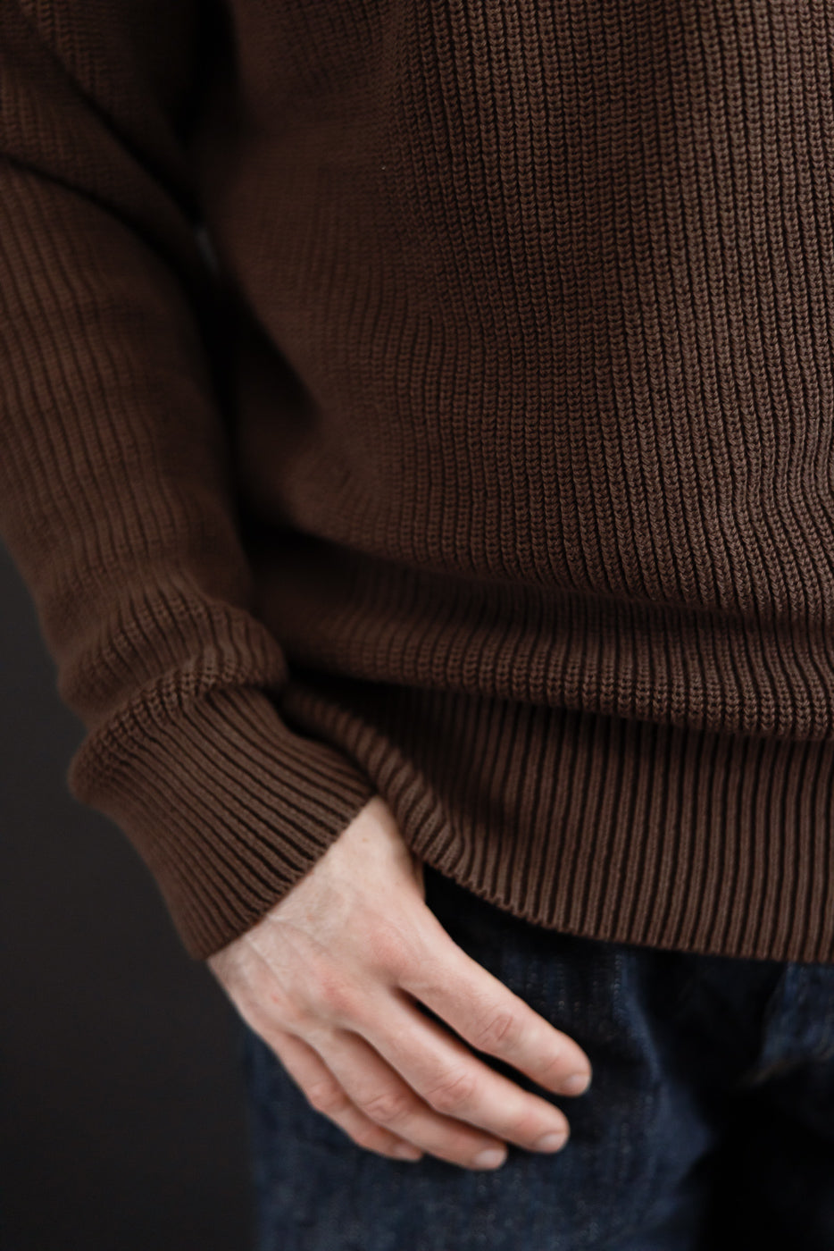 Close-up of the front hem and ribbed texture of a brown knit sweater on a male model.
