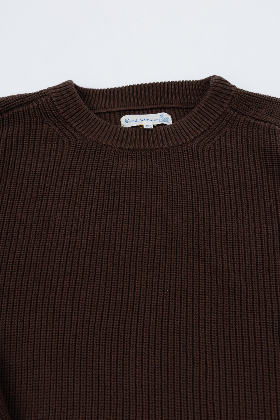 Close-up front view of a brown ribbed knit crewneck sweater showing the collar and tag detail.