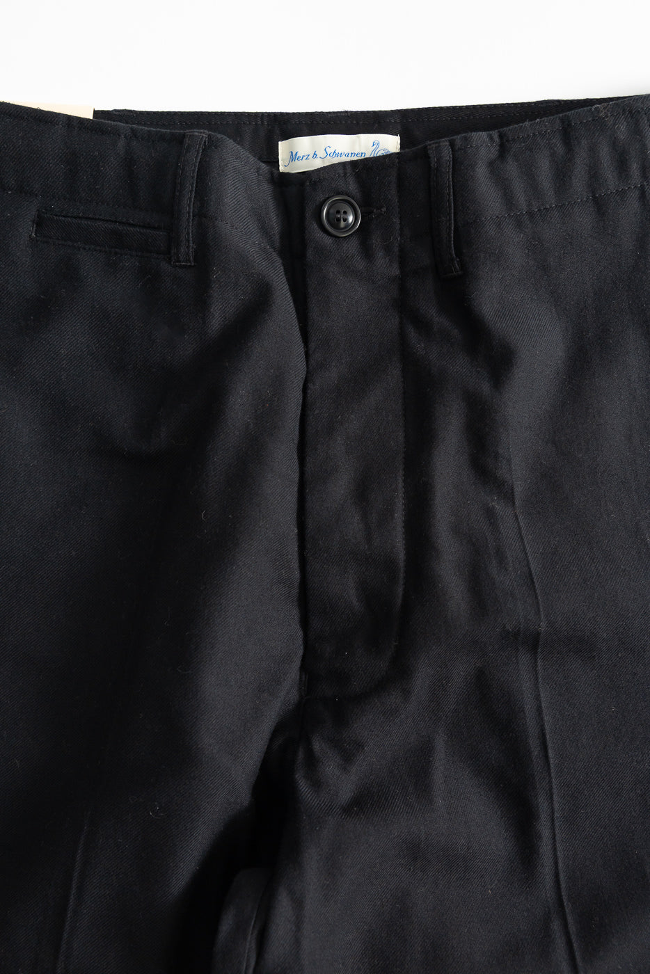 Close-up front detail of deep black wool-cotton worker chino showing waistband, button, and pocket.