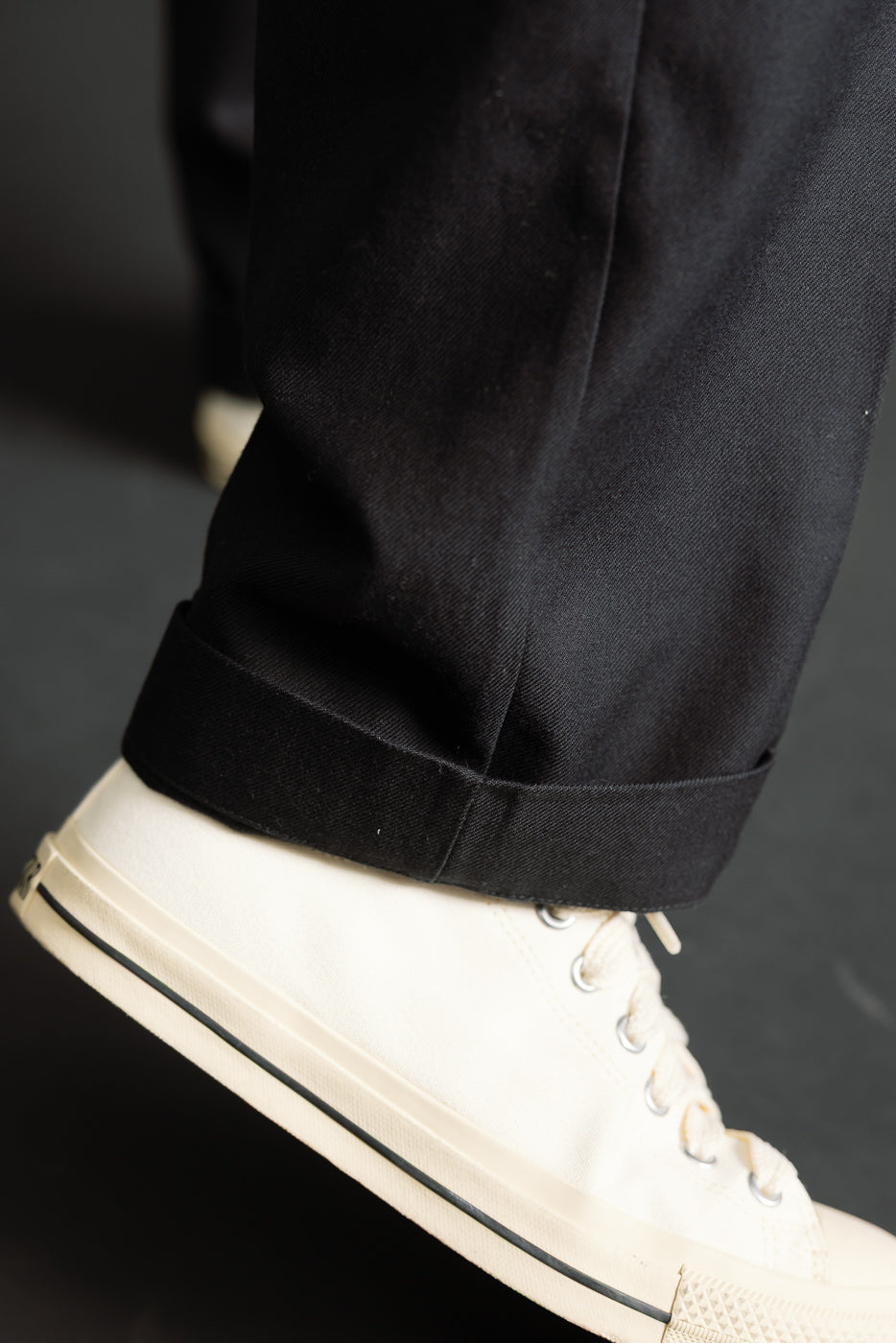 Close-up of male model’s lower leg showcasing deep black chino hem with turned cuff, side view.