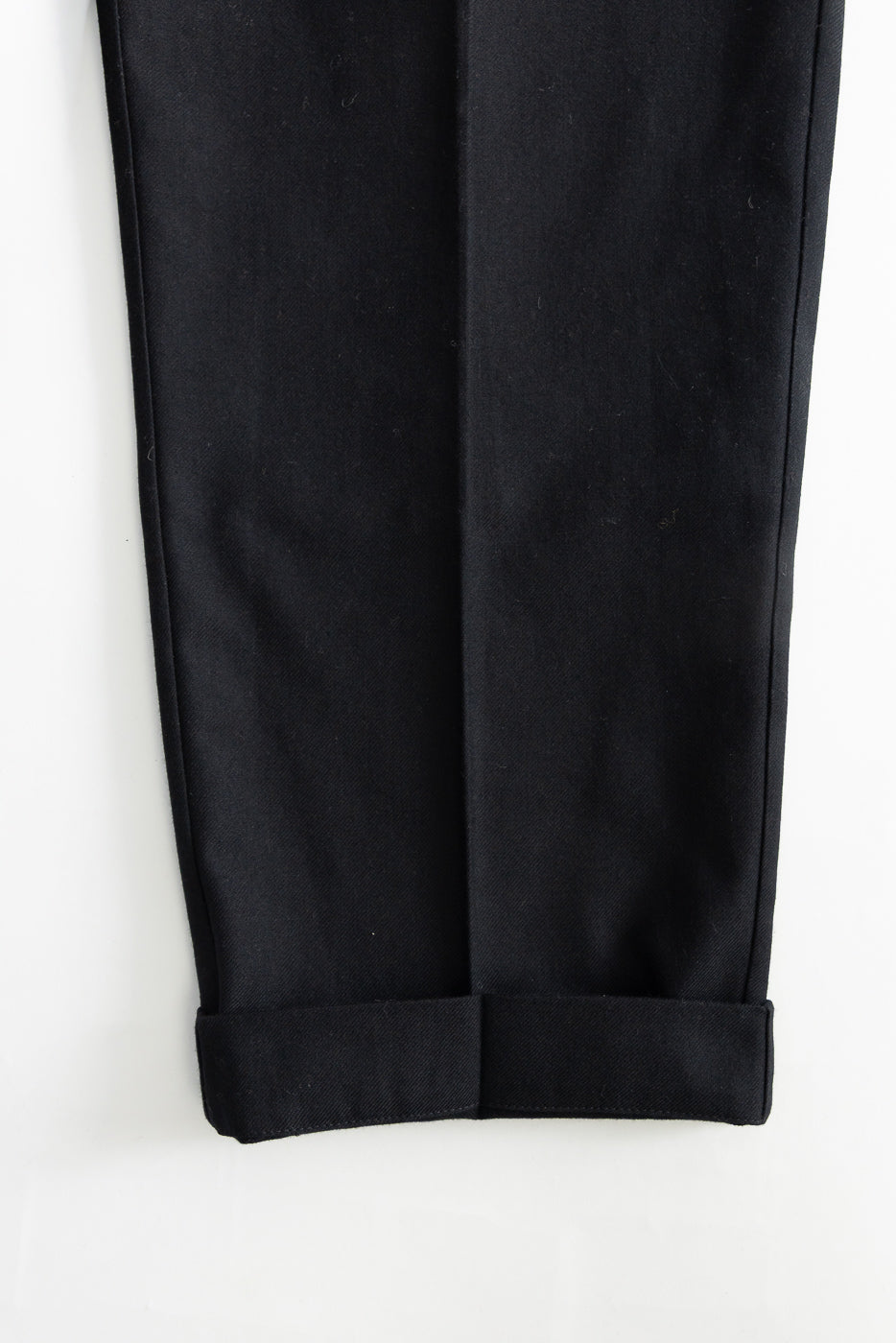 Close-up of deep black wool cotton worker chino front cuffs, showing fabric texture and hem