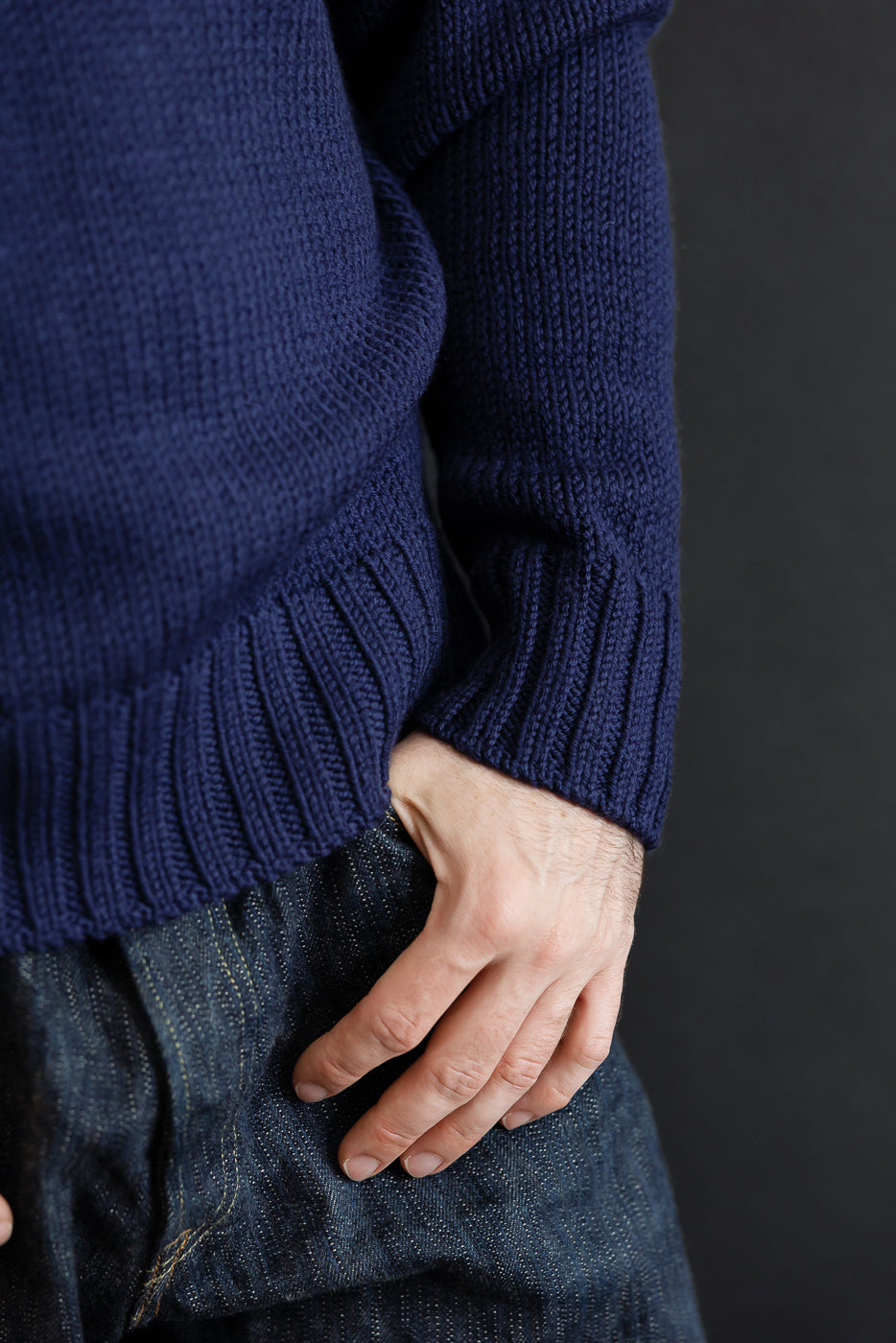 Close-up of the side and ribbed hem of a navy blue knit sweater and dark selvedge denim jeans.