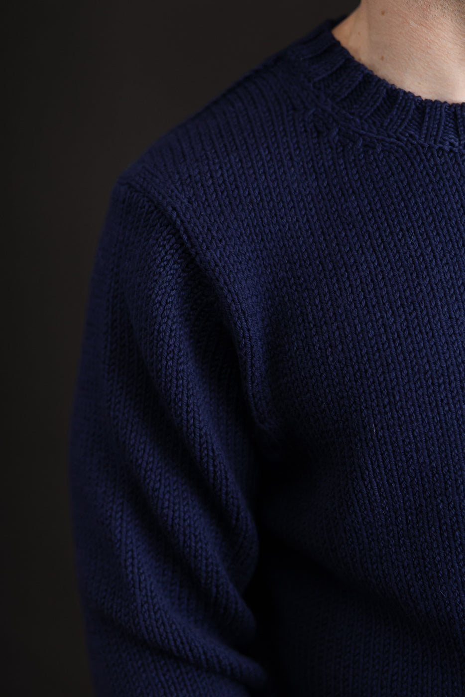 Close-up of the navy blue ribbed knit texture and crewneck collar of a men's sweater.