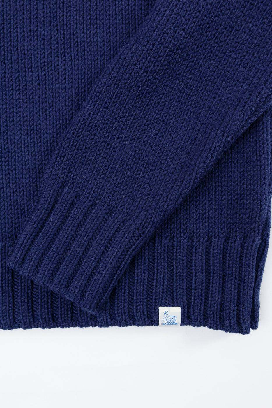 Close-up of the ribbed hem and sleeve cuff of a navy blue knit sweater showing a white swan tag.