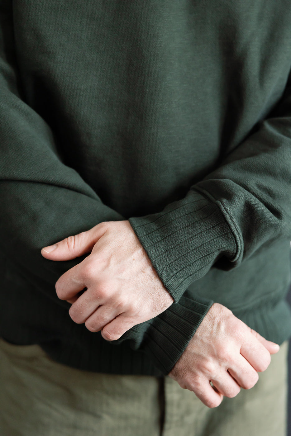 Close-up of male model’s arms in forest green heavyweight fleece cotton sweatshirt, front view, showing ribbed cuffs; model is 5'9