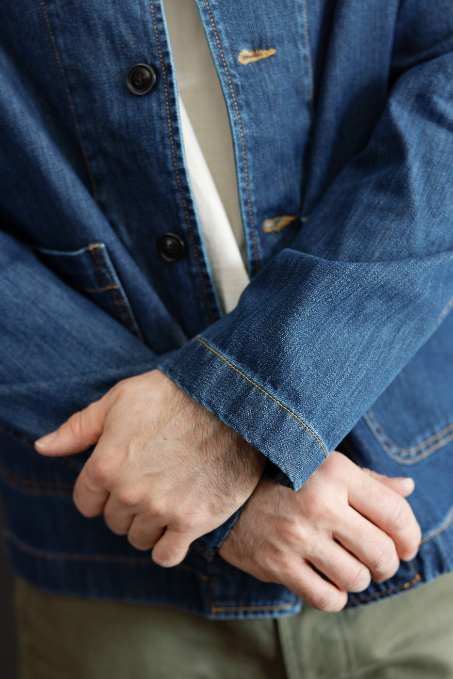 Close-up of a person wearing the JKT08DN.520MB - Cropped Worker's Denim Jacket, showcasing its vintage dark wash, corozo nut buttons, and two front pockets over a white shirt and olive-green pants.