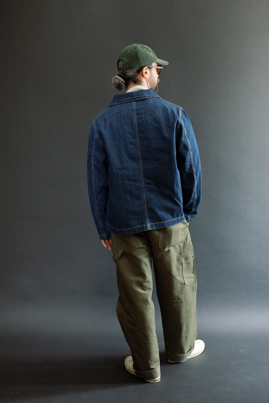 Person wearing the JKT08DN.520MB Cropped Worker's Denim Jacket in indigo mid blue, styled with olive-green cargo pants and white sneakers, showcasing the jacket's cropped cut and vintage dark wash.