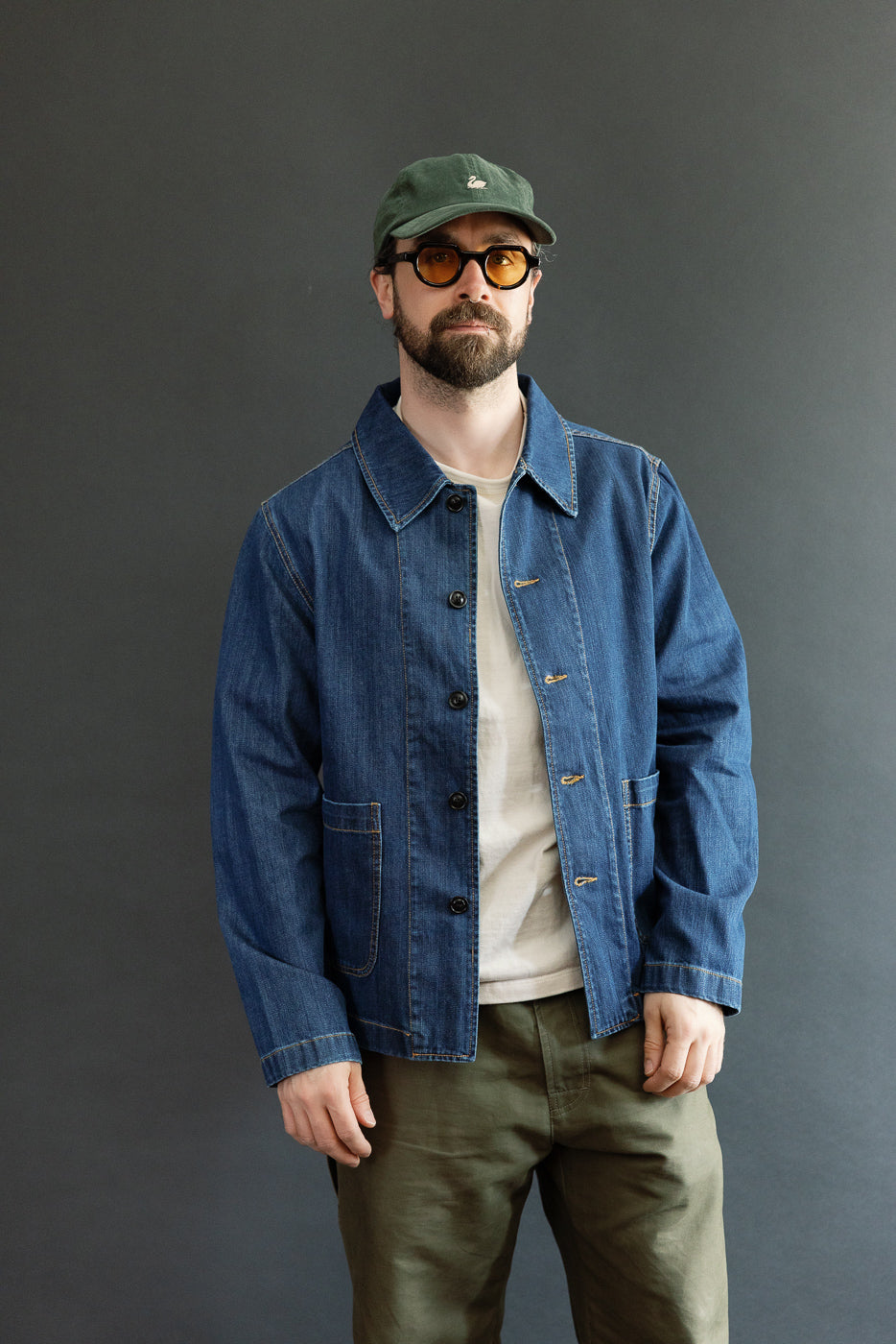 Man wearing JKT08DN Cropped Worker's Denim Jacket, showcasing its cropped fit, vintage wash, and front pockets. Styled with olive trousers, embodying Dant's premium workwear aesthetic.