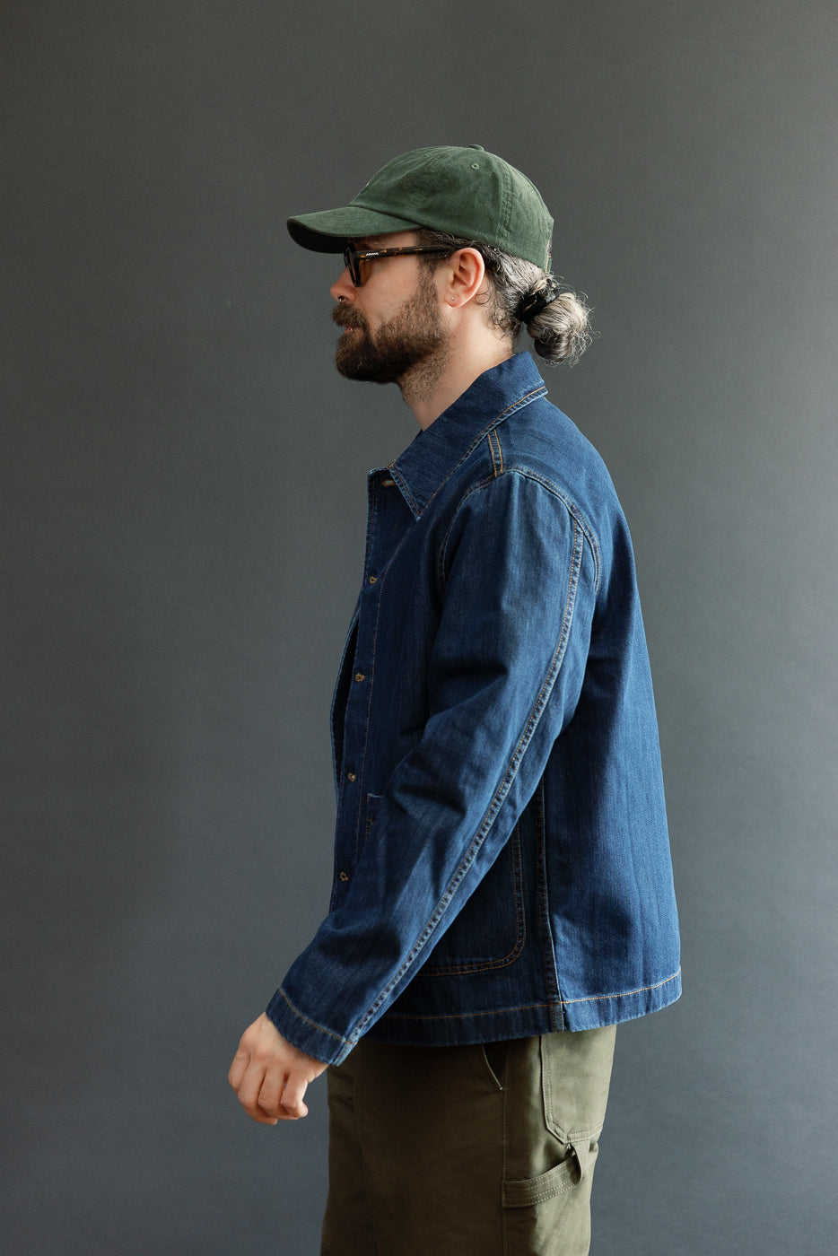 Man in profile wearing the JKT08DN Cropped Worker's Denim Jacket, showcasing its vintage dark wash, cropped cut, classic collar, and front pockets, embodying Merz b. Schwanen's refined workwear aesthetic.