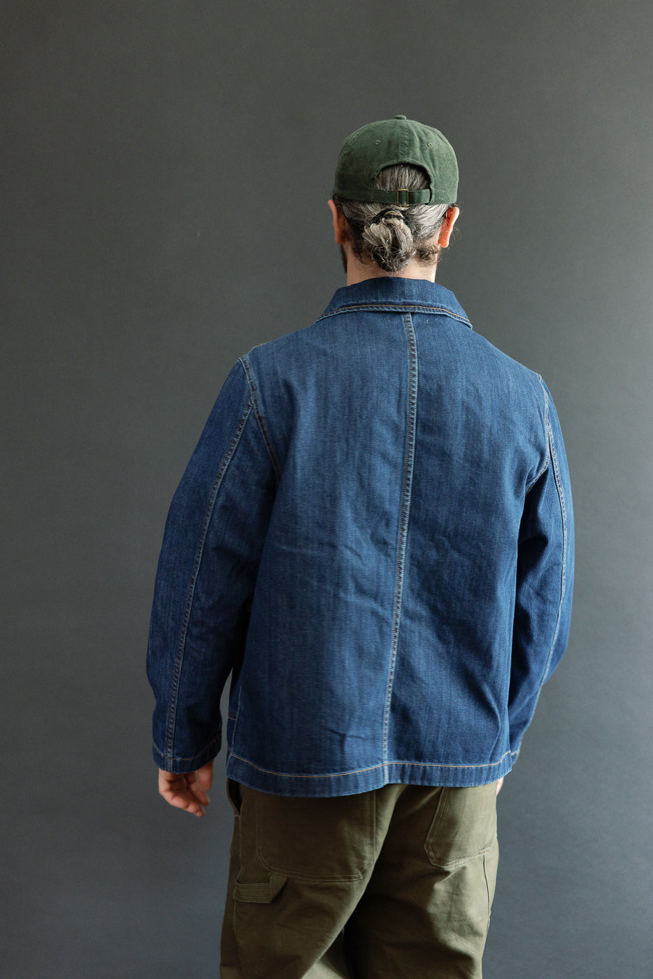 A person wearing the JKT08DN Cropped Worker's Denim Jacket, showcasing its vintage dark wash, cropped cut, and corozo nut buttons, styled with olive cargo pants for a workwear-inspired look.