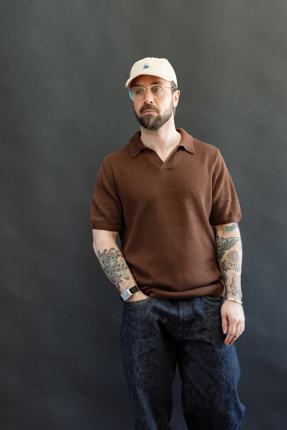 Man wearing the KNITPOLO02.192.7 - Cotton Short Sleeve Polo Shirt in chocolate, featuring a relaxed fit, plant-based knit, and swan embroidery, styled with jeans and accessories for a casual look.
