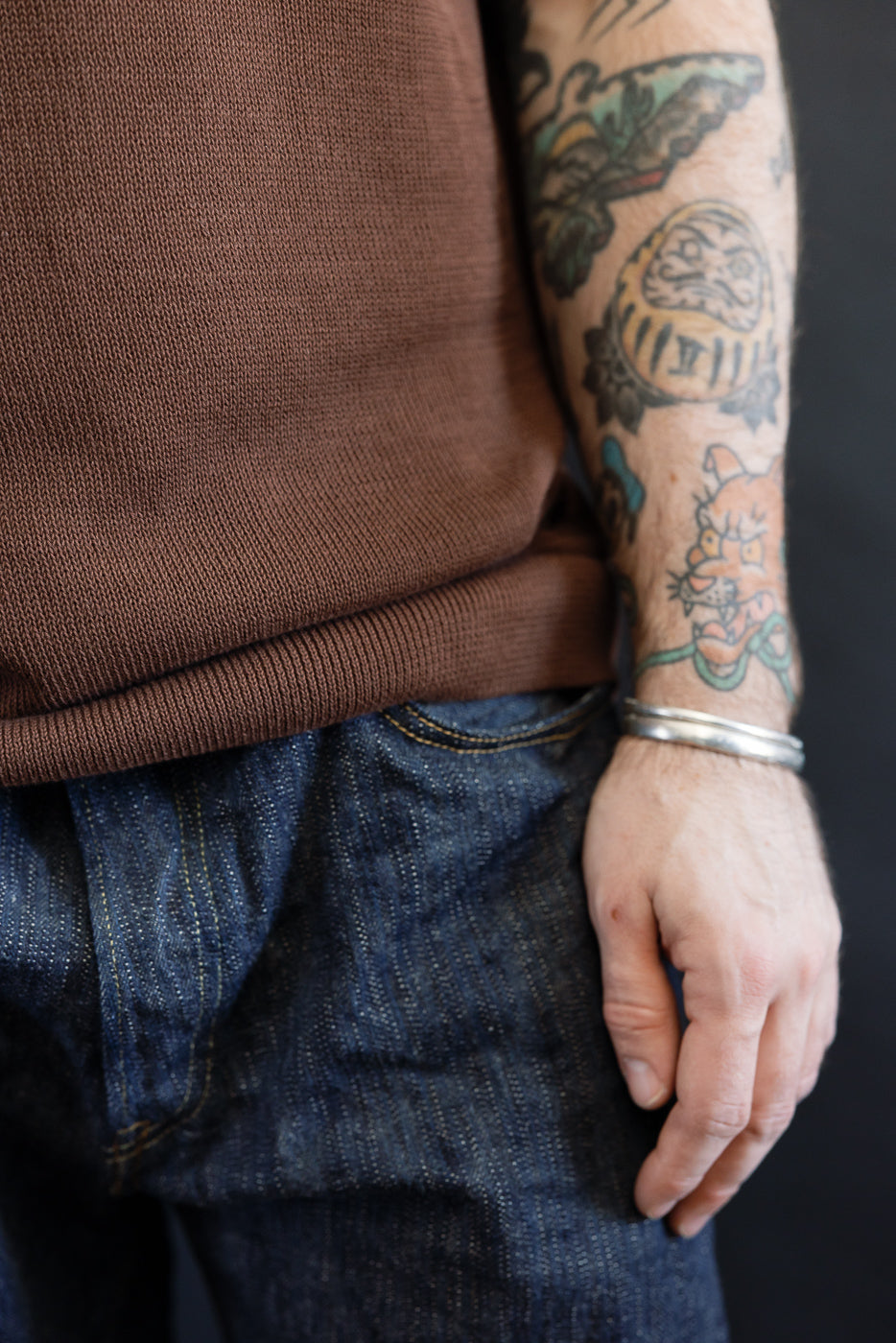 Close-up of a person wearing the Merz b. Schwanen KNITPOLO02 Cotton Short Sleeve Polo Shirt, showcasing its relaxed knit texture and simple silver bracelet, with colorful tattoos visible on the forearm.