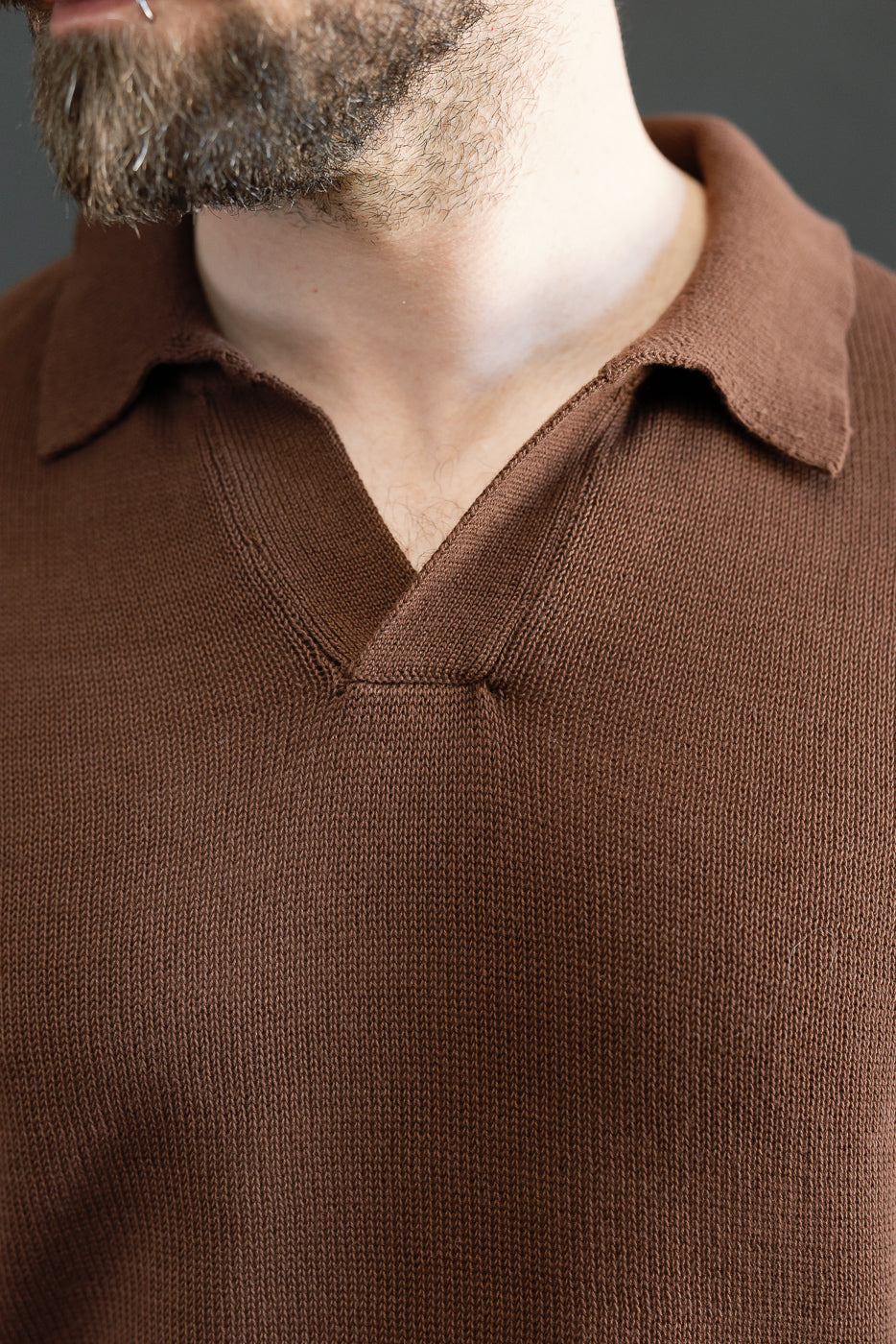 Close-up of KNITPOLO02.192.7 - Cotton Short Sleeve Polo Shirt, highlighting its textured, organic cotton knit and relaxed V-neck, worn by a model with a trimmed beard and lip-ring.