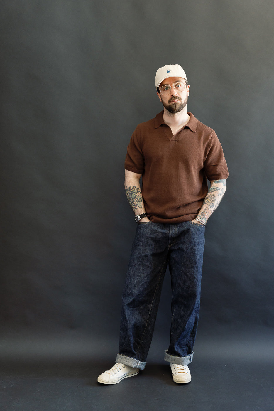 A bearded man models the KNITPOLO02.192.7 - Cotton Short Sleeve Polo Shirt in Chocolate, showcasing its soft, relaxed organic cotton knit and small open V-neck, embodying Dant's premium menswear style.