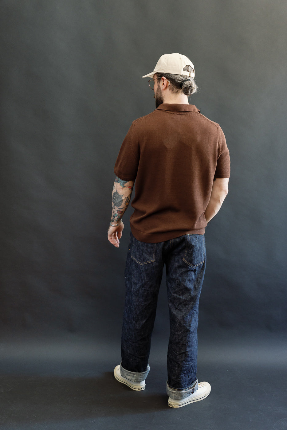 A man models the KNITPOLO02.192.7 - Cotton Short Sleeve Polo Shirt, All Plant Based - Chocolate, showcasing its relaxed fit, organic cotton knit, and subtle swan embroidery above the hem.