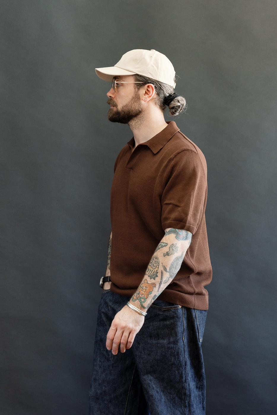 Bearded man in profile wearing the KNITPOLO02.192.7 - Cotton Short Sleeve Polo Shirt, showcasing its relaxed fit and unique V-neck, paired with tattoos and accessories.