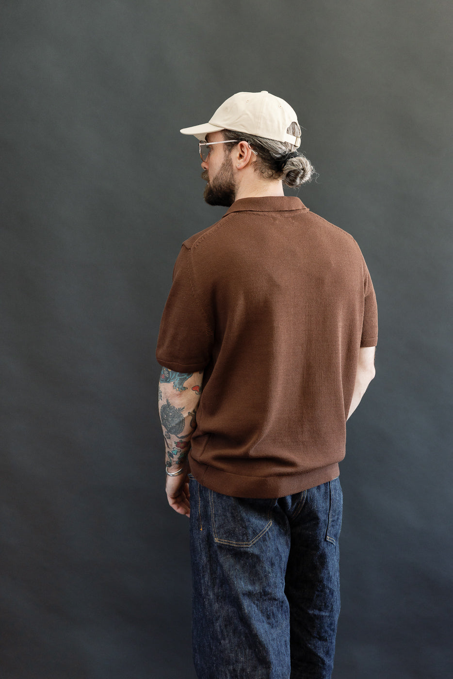 A man models the KNITPOLO02.192.7 - Cotton Short Sleeve Polo Shirt, featuring a soft, relaxed plant-based knit and a small swan embroidery above the hem, styled with dark denim jeans.