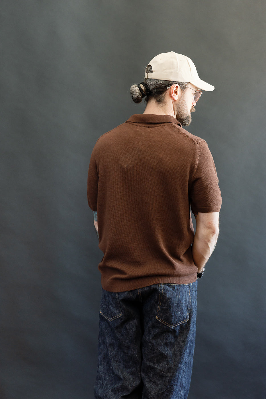 A man wears the KNITPOLO02.192.7 Cotton Short Sleeve Polo Shirt, featuring a relaxed knit texture and small open V-neck, highlighting its sustainable, plant-based design.