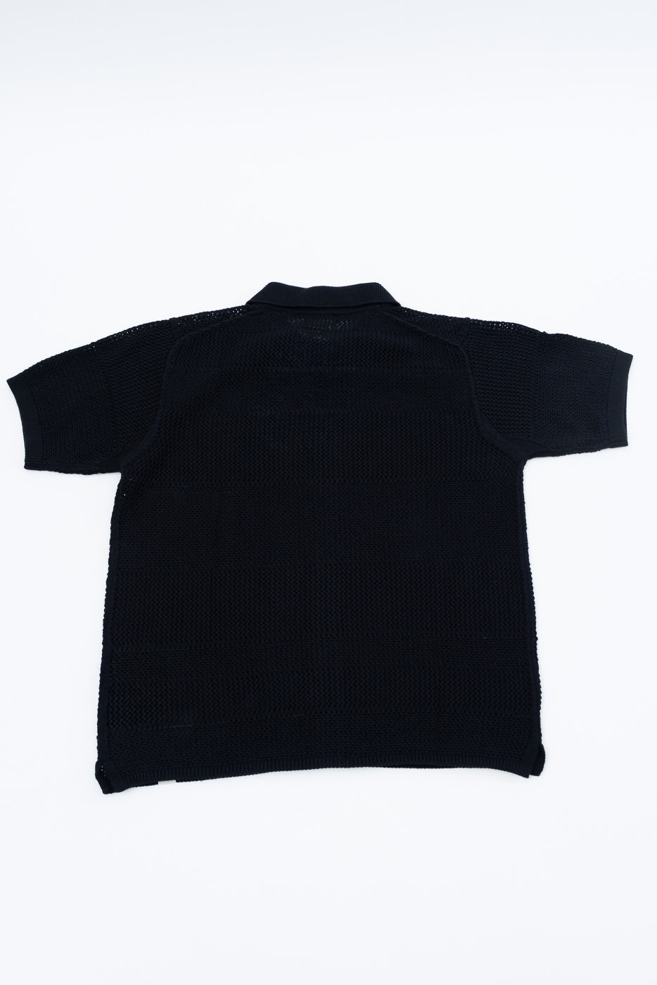 Flat lay of the back of a deep black crochet cotton short sleeve shirt, showing knit texture.