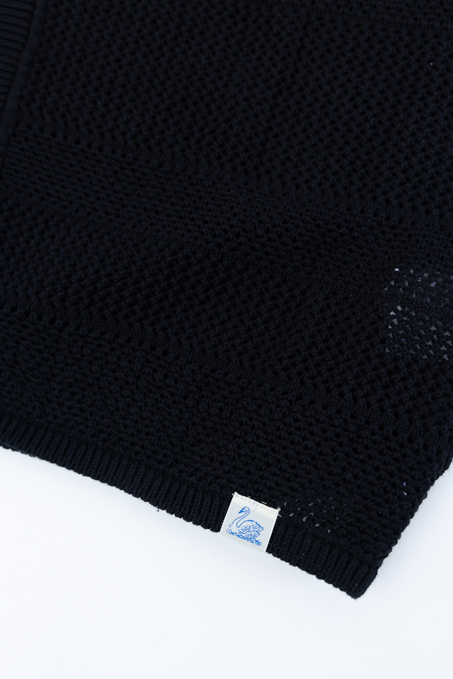 Close-up of deep black crochet cotton knit shirt hem, focusing on textured fabric and woven tag at bottom front.