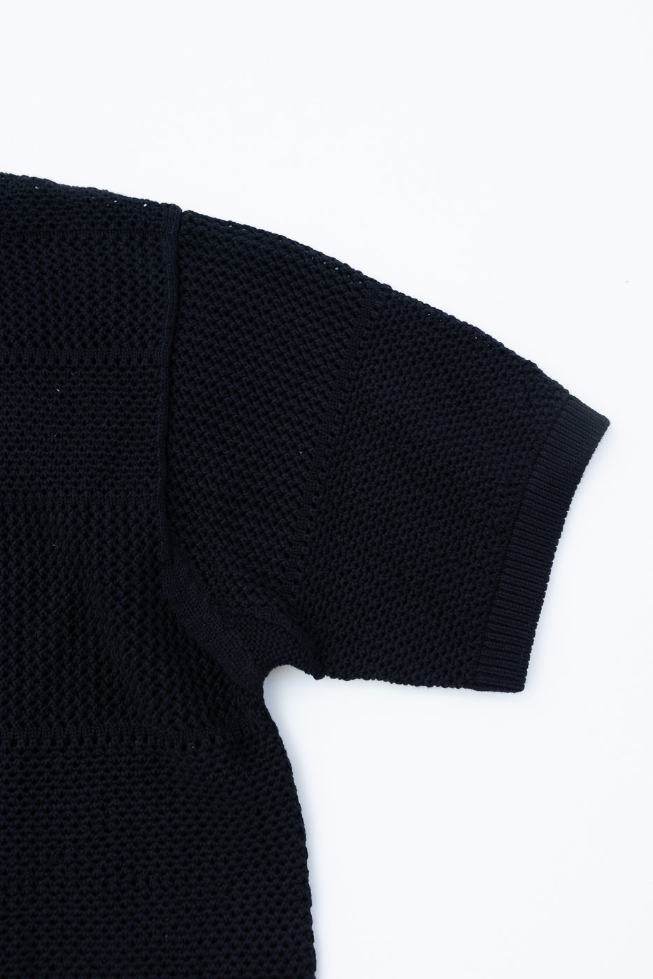 Close-up of front right sleeve on deep black crochet cotton short sleeve shirt, showing knit texture and ribbed cuff.