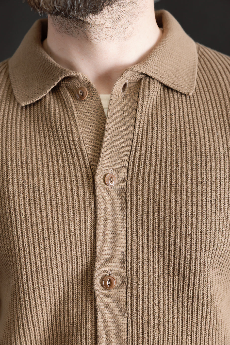 Close-up of front chest and collar of men's ribbed cotton knit shirt, showing button details. Male model, 5'9