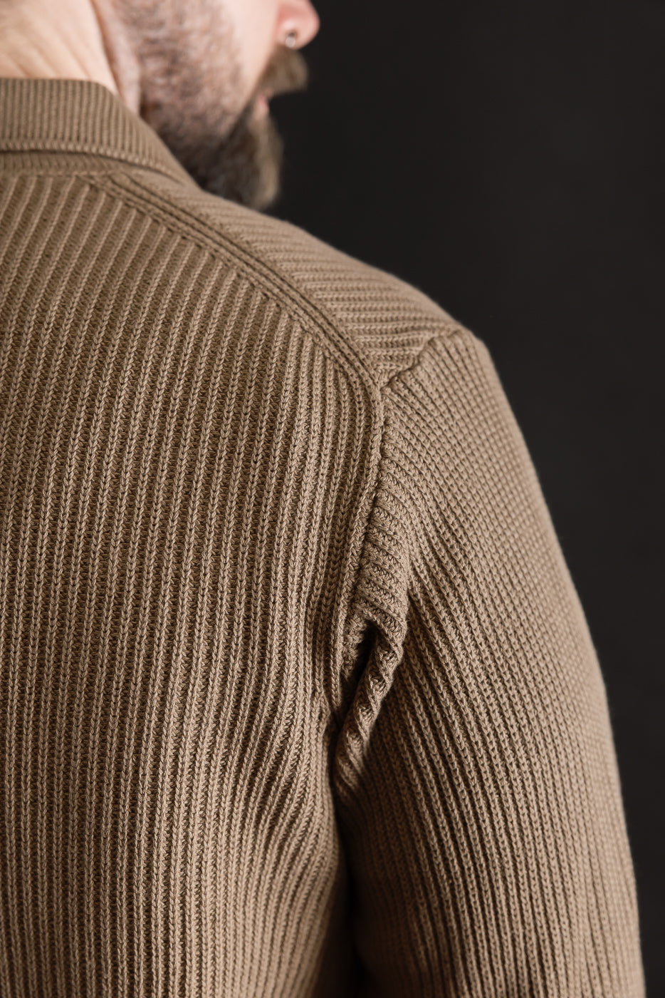 Close-up of the back right shoulder of a ribbed cotton long sleeve shirt on a male model, 5'9