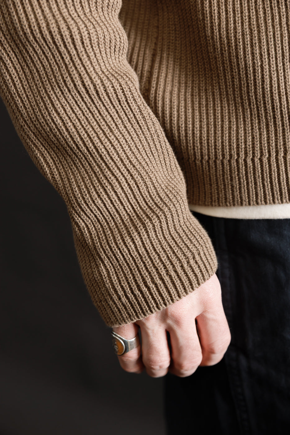 Close-up of male model's left arm in a ribbed cotton long sleeve shirt, showing sleeve texture and cuff, side view. Model is 5'9