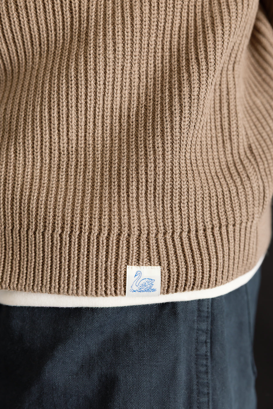 Close-up of front hem on men's ribbed cotton long sleeve shirt in grain color, swan tag visible.