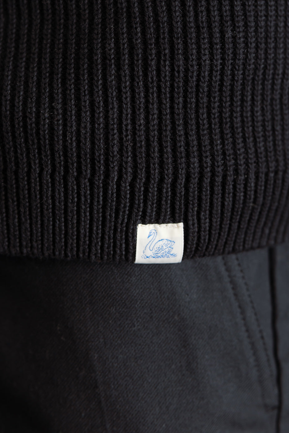 Close-up of hem detail on ribbed black cotton long sleeve shirt, front side, small swan tag visible.
