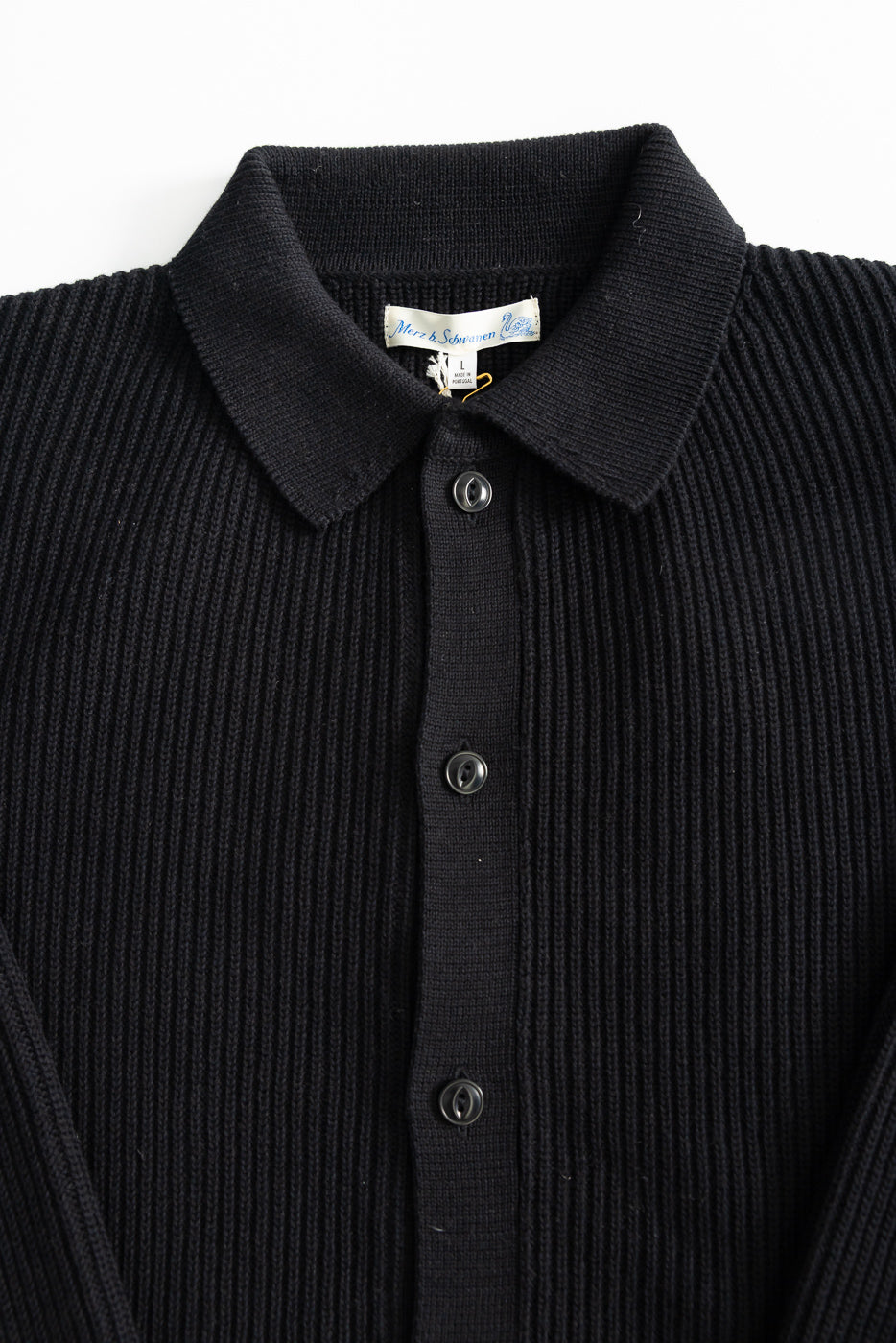Close-up front of ribbed black cotton long sleeve shirt, showing collar, buttons, and texture.