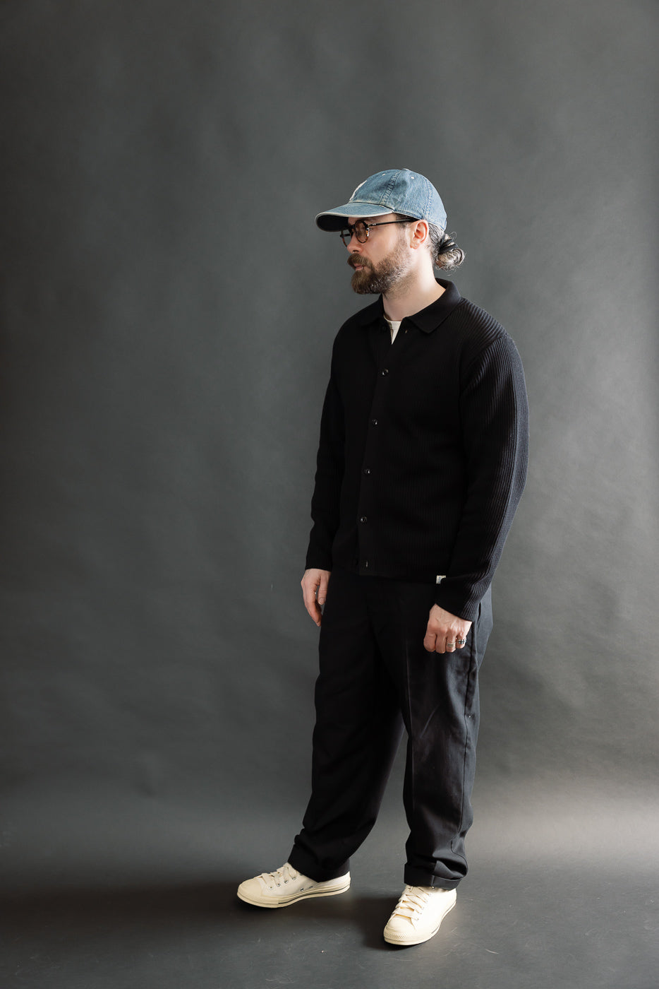 Full body, left side view of male model 5'9 165lbs athletic build wearing deep black ribbed cotton long sleeve knit shirt with button front