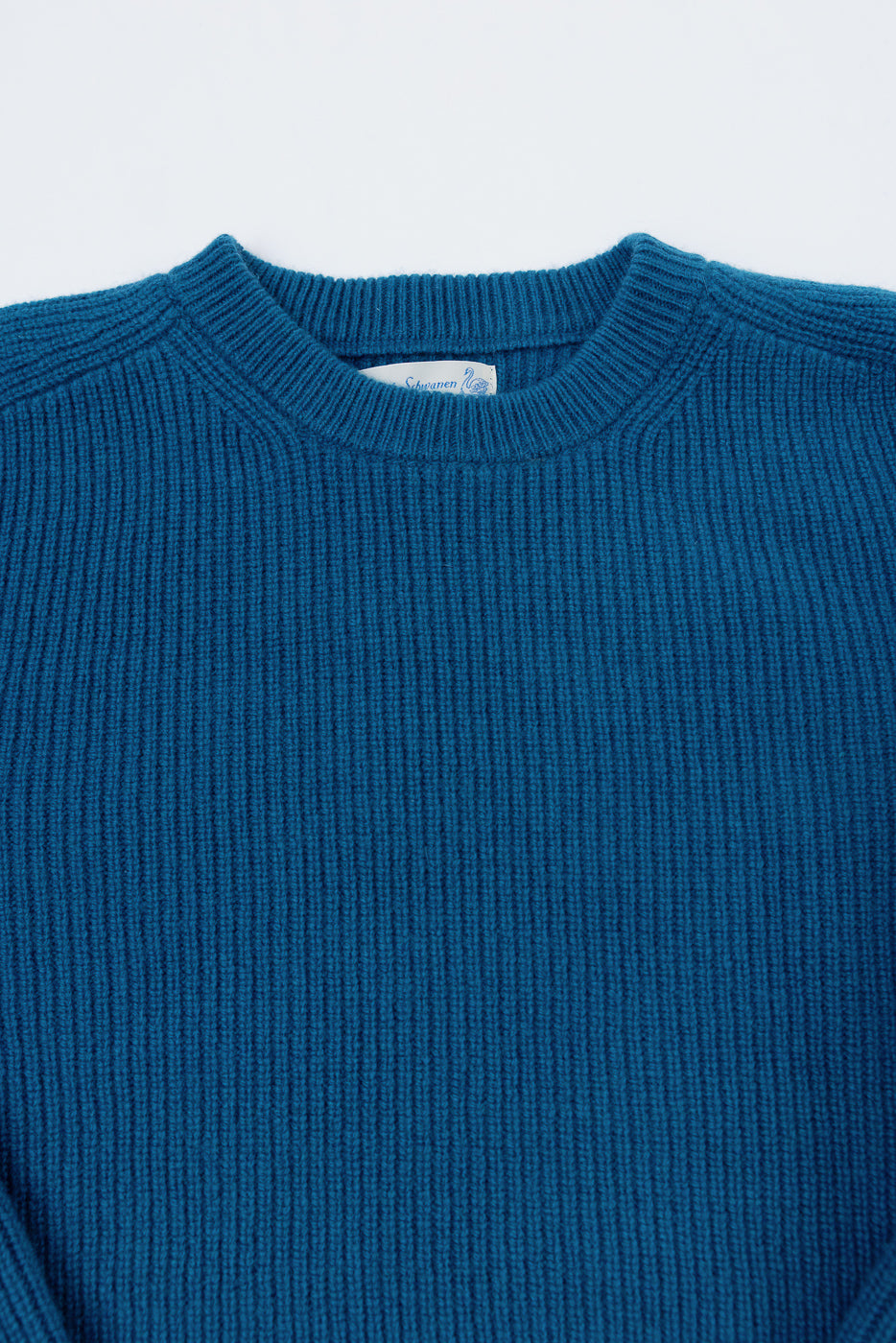 Close-up of the front neckline and ribbed texture of a blue sweater with a visible neck tag.