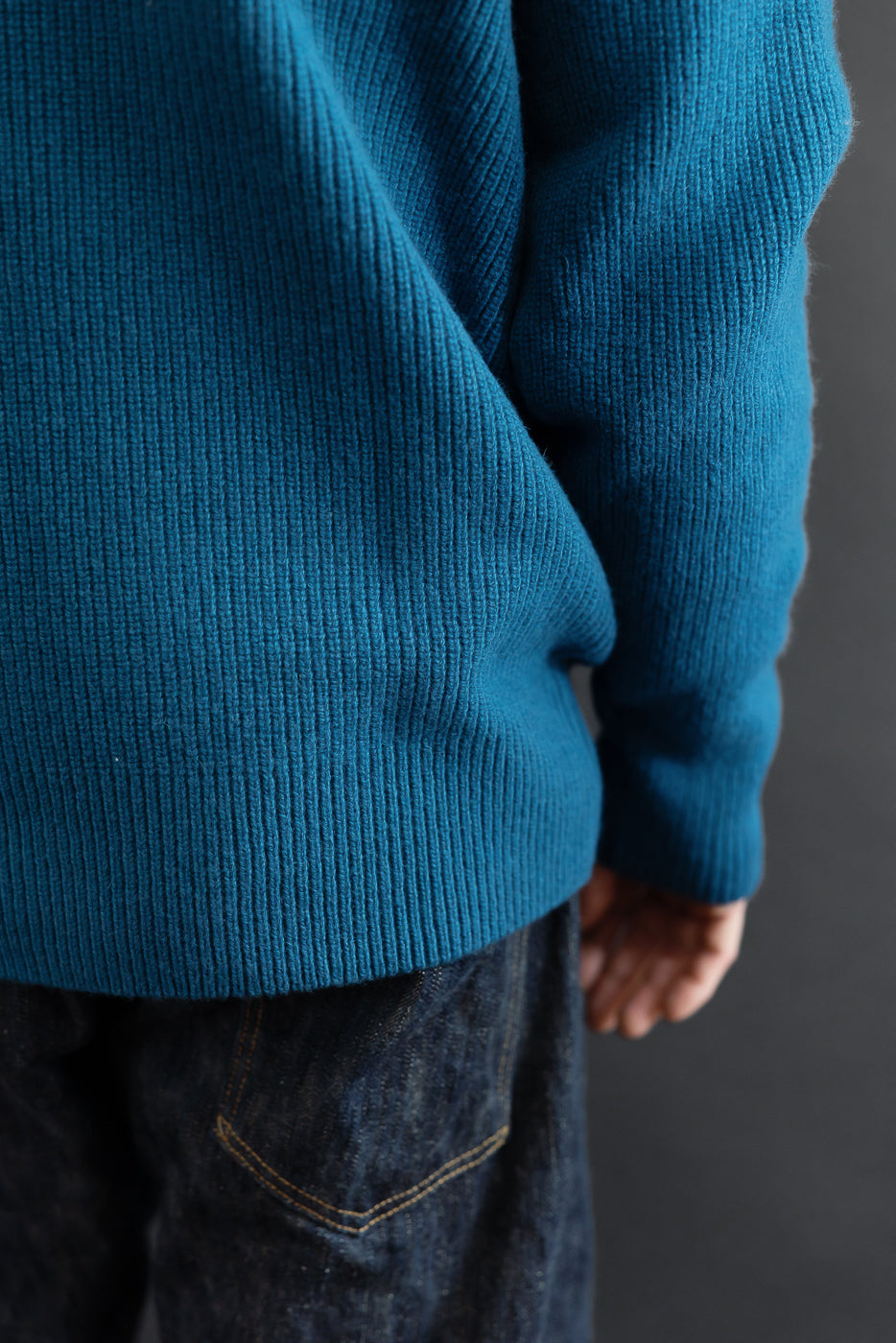 Close-up of the side and back of a teal ribbed knit sweater worn by a male model.