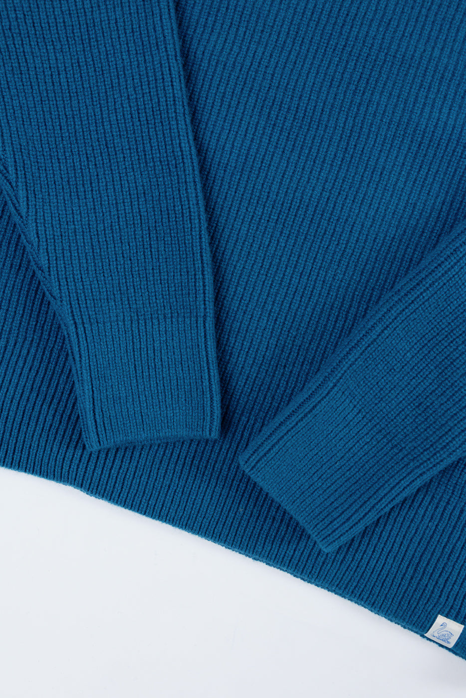 Close-up of the front ribbed texture and sleeve cuffs of a teal blue knit sweater.