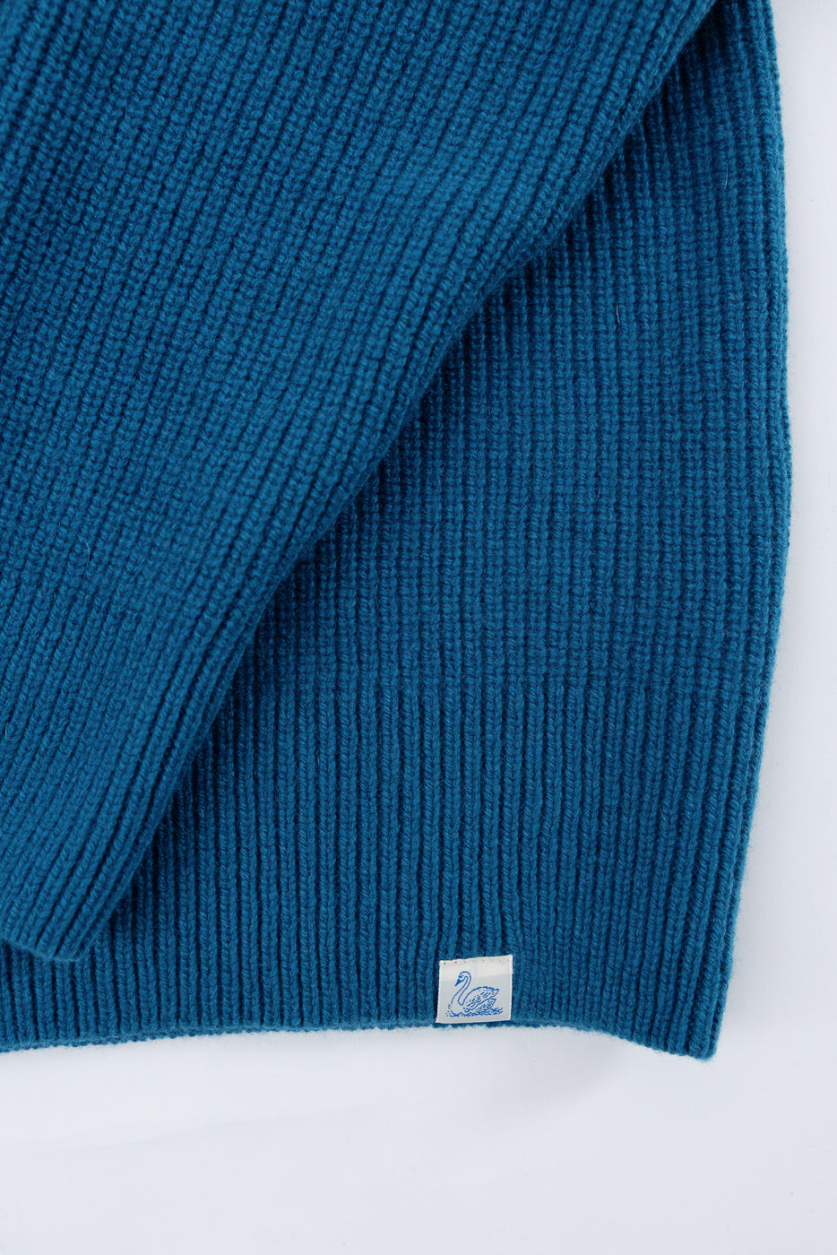 Close-up of the front hem of a blue ribbed knit scarf featuring a small white brand tag.