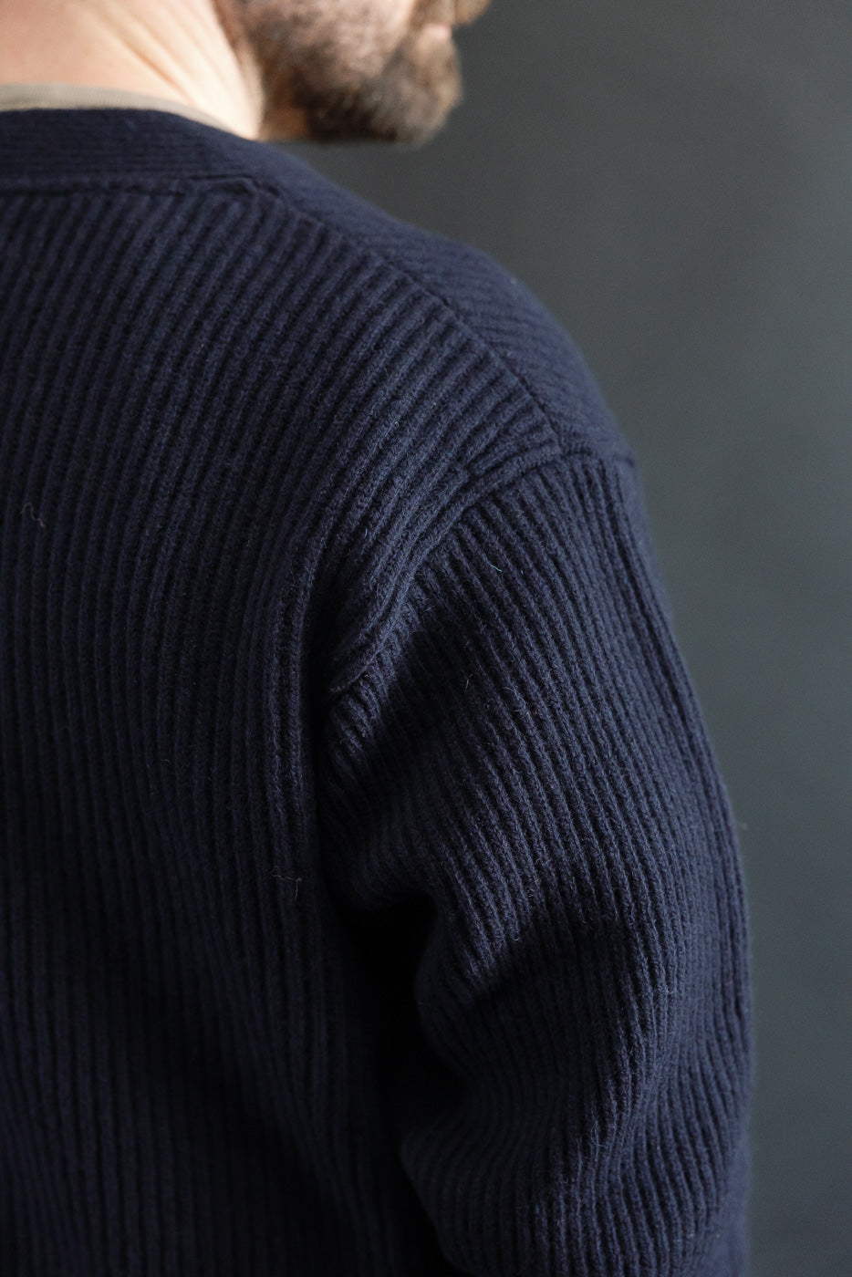 Close-up of back shoulder and sleeve on male model wearing navy Merz B. Schwanen Merino wool cashmere cardigan, showing ribbed knit texture.