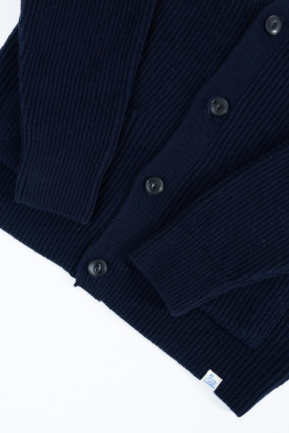 Close-up of Merz b. Schwanen navy merino wool cashmere cardigan front, showing buttons, ribbed texture, and hem tag