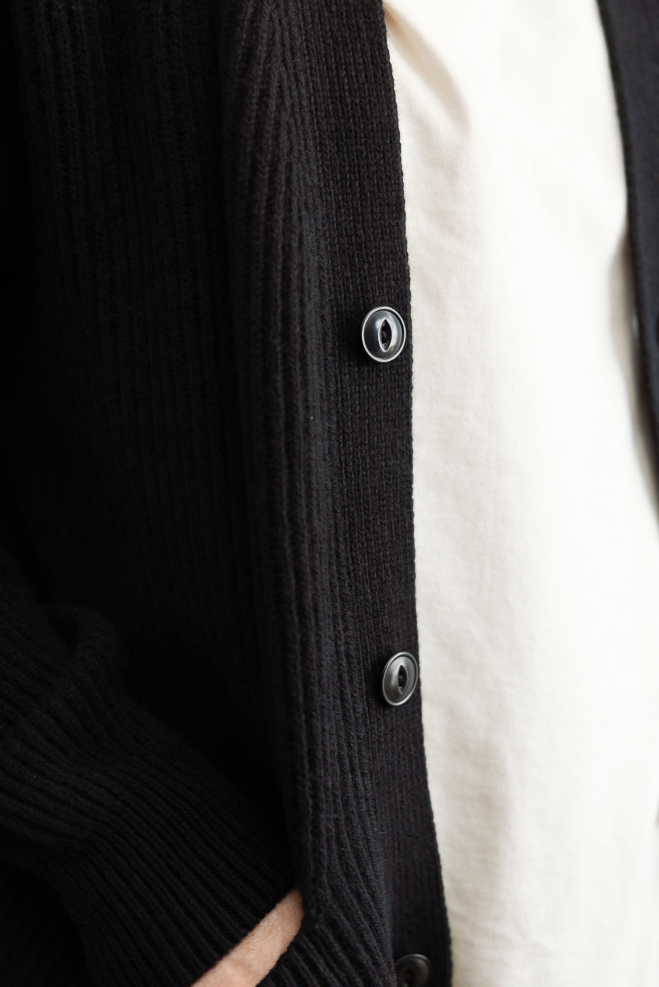 Close-up of the front right side of a black ribbed cardigan with buttons on a male model.