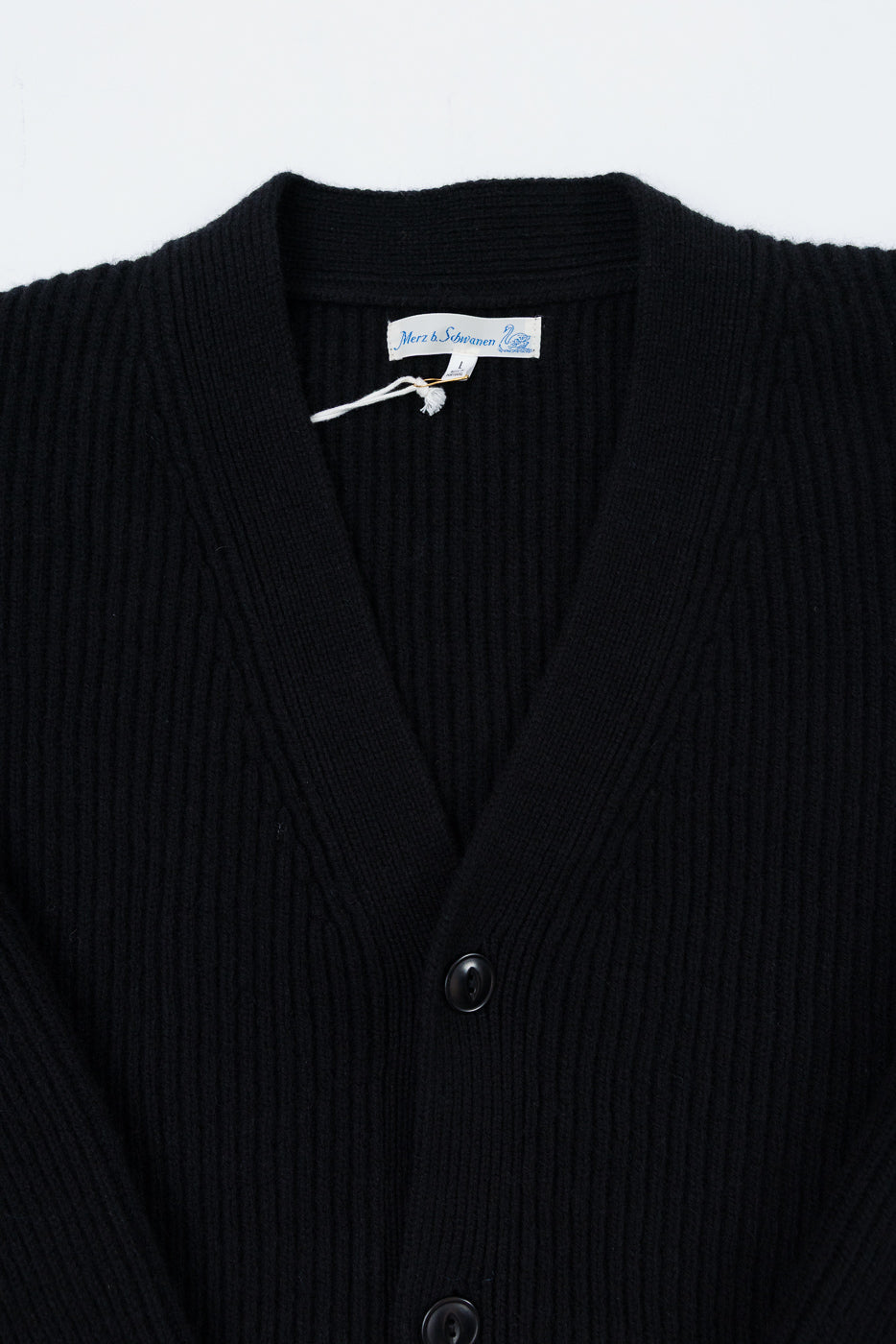 Close-up front view of a black ribbed cardigan showing the v-neck collar, tag, and buttons.