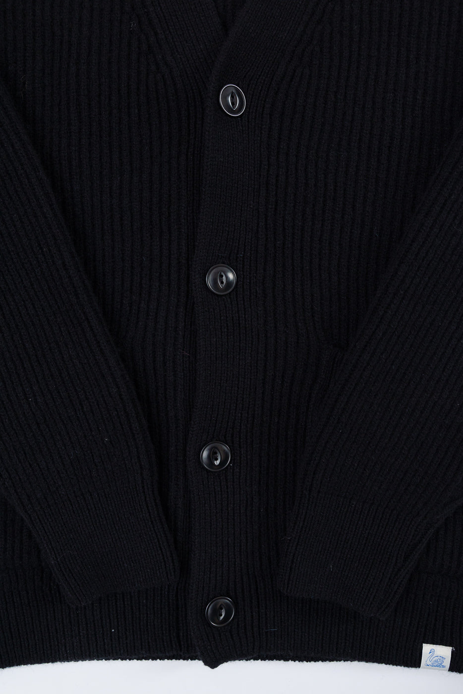 Close-up of the front of a black ribbed knit cardigan showing buttons and fabric texture.