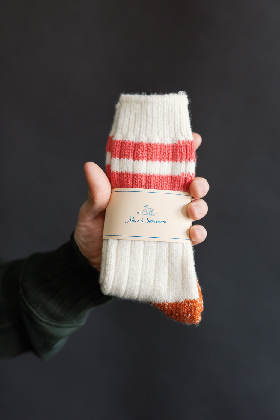 Close-up of Merz b. Schwanen extra fine merino wool socks in nature and ink color, front view, held by hand showing ribbed texture and striped design at Dant casual apparel store.