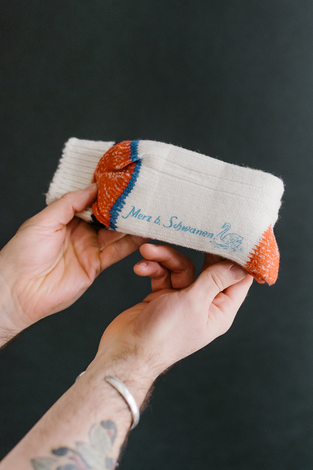 Close-up of Merz b. Schwanen extra fine merino wool socks, front side, logo visible, held by hand