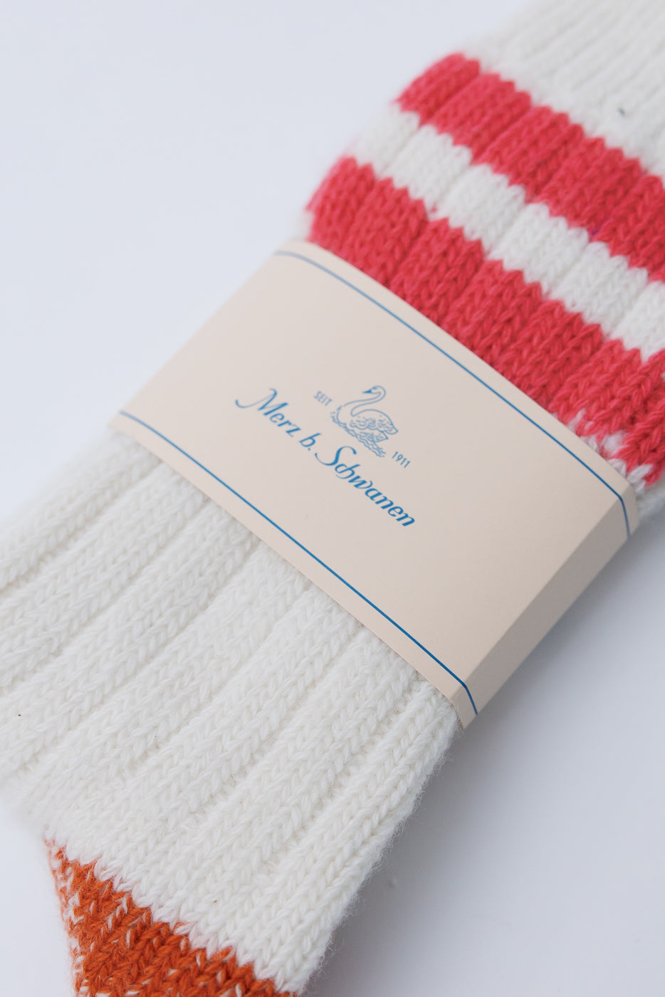 Close-up front view of Merz b. Schwanen extra fine merino wool socks in white with red stripes and orange toe, showcasing ribbed knit texture and brand tag, Dant contemporary casual accessories.