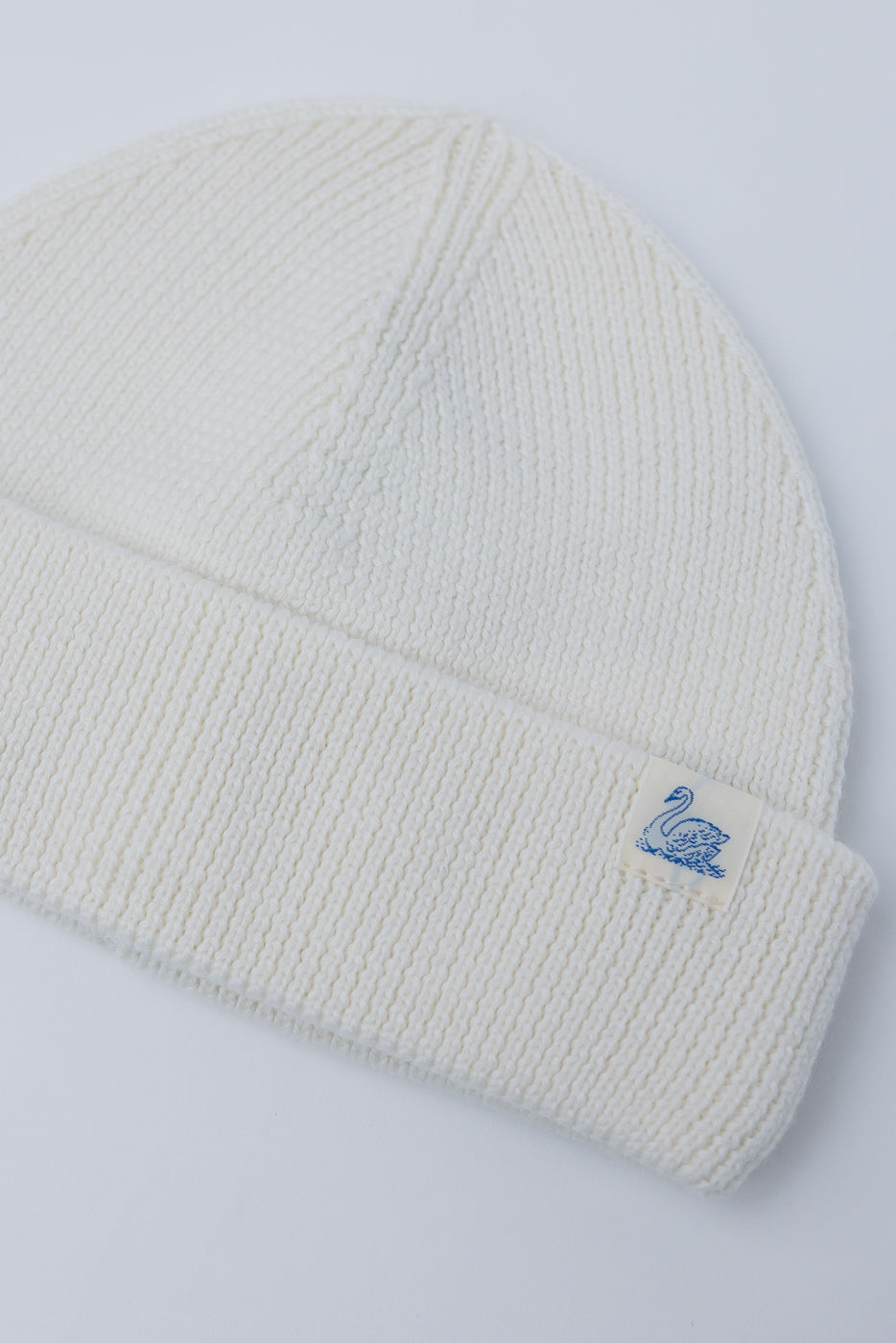 Close-up front view Merz B. Schwanen ribbed merino wool watch cap in natural with swan tag.