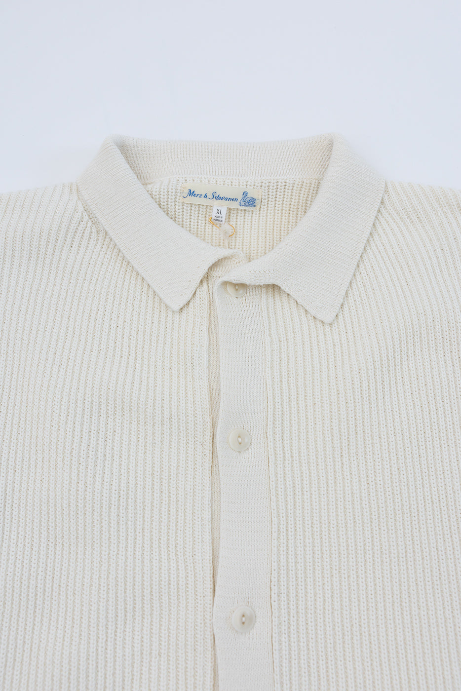 Close-up of front of cream ribbed cotton knit short sleeve shirt, showing buttons, collar, and fabric texture.